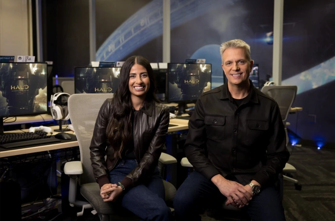 Asha Sharma y Matt Booty sentados en una oficina de Xbox, con monitores y un mural de Halo de fondo