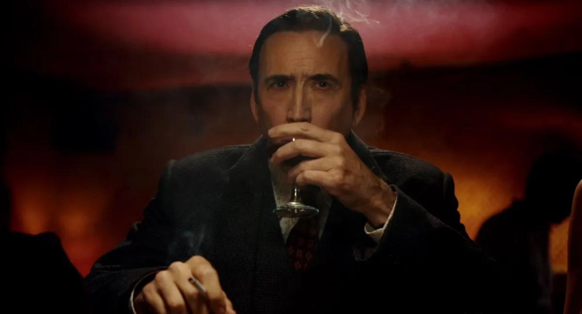 Nicolas Cage como Ben Reilly bebe de una copa con un cigarrillo encendido en la otra mano, en Spider-Noir