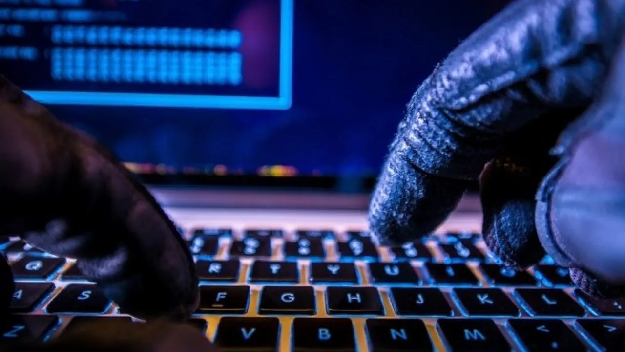 Manos con guantes escribiendo en el teclado retroiluminado de una notebook - hackeo