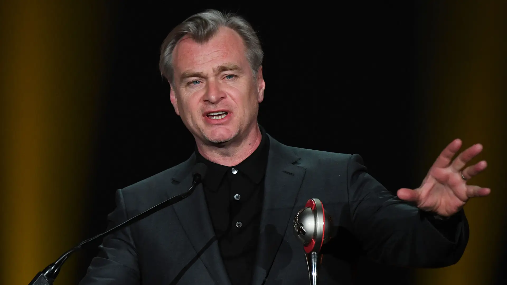Christopher Nolan hablando frente a un micrófono durante un evento público