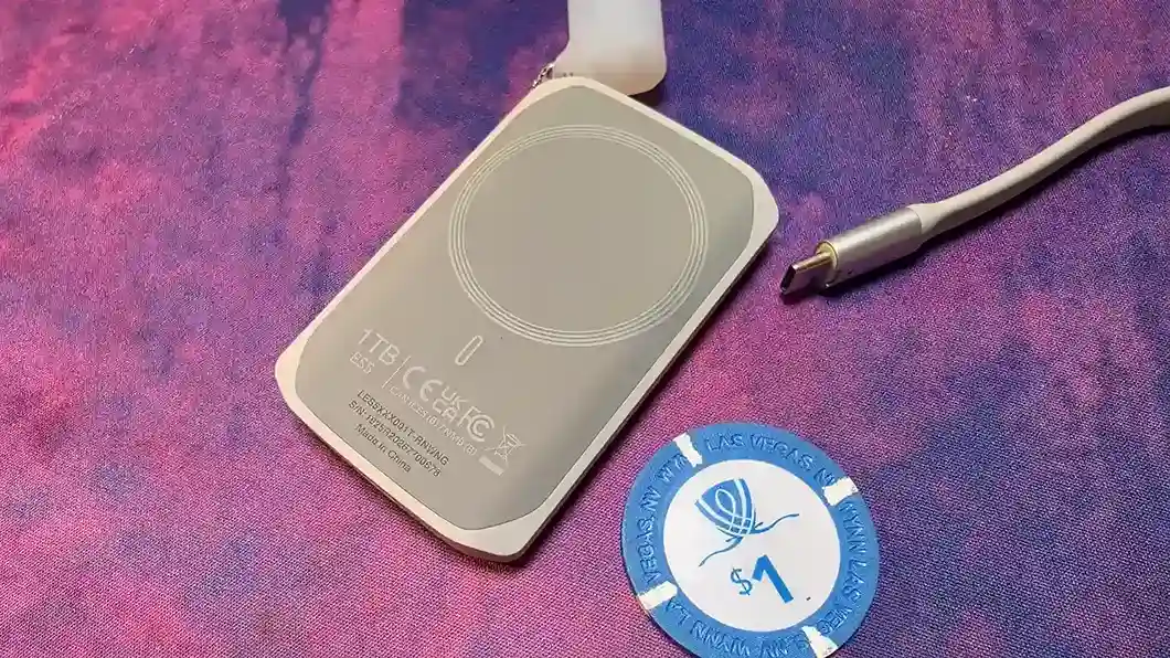 Dorso de la Lexar ES5 de 1 TB en primer plano, con el anillo magnético y las certificaciones grabadas, junto a una ficha de casino de un dólar que sirve de referencia de tamaño