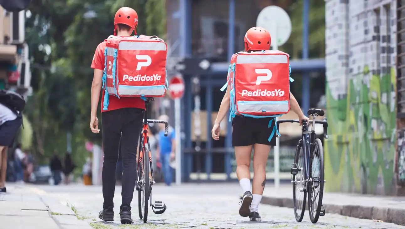 Repartidores de PedidosYa caminando con sus mochilas en una calle de Argentina