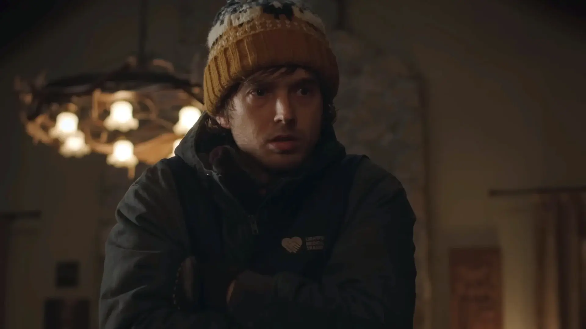 Primer plano de Bryan, protagonista de Resident Evil: Noche Cero, con gorro de lana y campera de mensajero medico dentro de una casa
