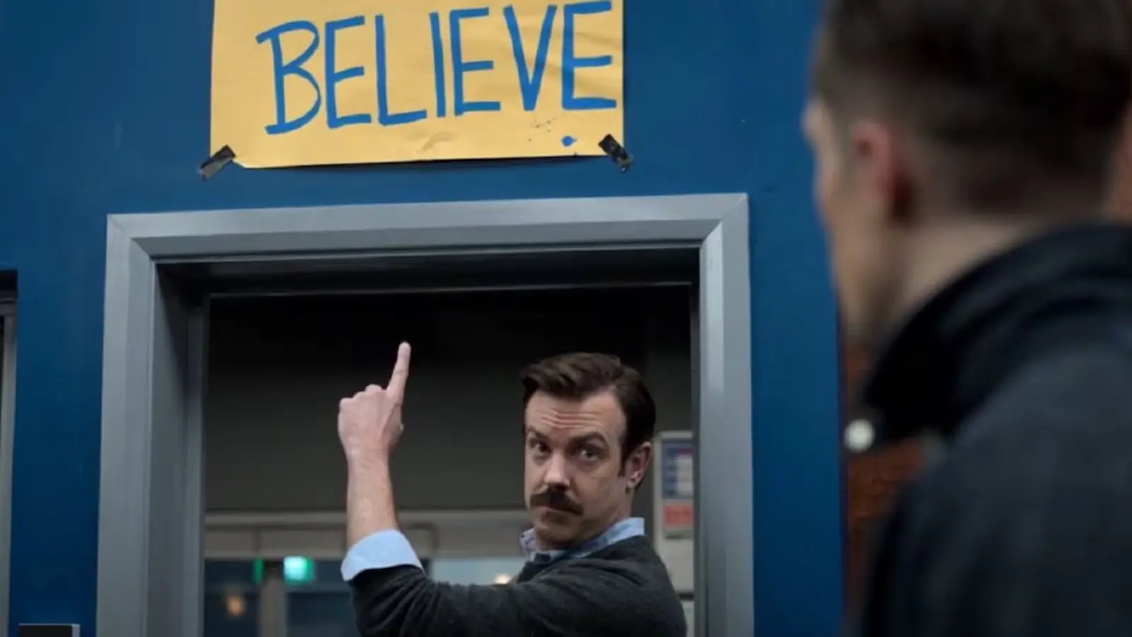 Ted Lasso señala el cartel de Believe, la marca registrada de la serie de Apple TV