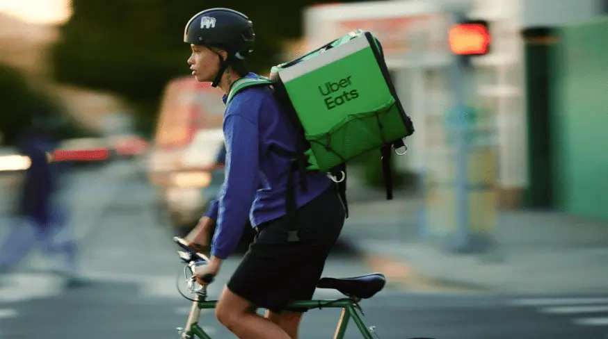 Repartidor de Uber Eats en bicicleta con la mochila verde en la ciudad