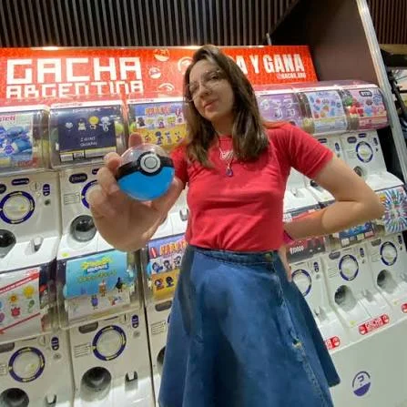 Chica sosteniendo una cápsula de Pokémon frente al cartel de Gacha Argentina en el pop-up de gashapones