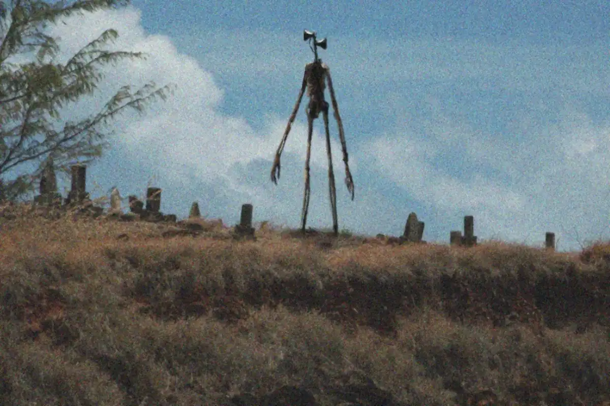 Siren Head, la criatura viral de Trevor Henderson, parada sobre una colina junto a un cementerio en el fotomontaje original del artista