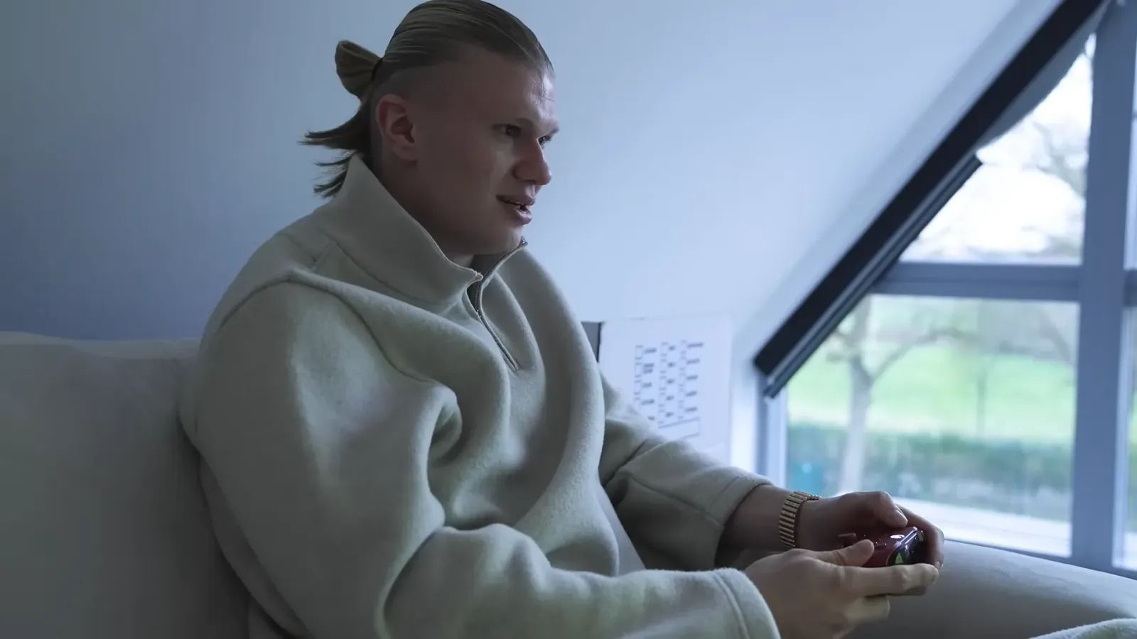 Erling Haaland sentado en un sillón con un joystick en la mano, jugando a la consola en su casa