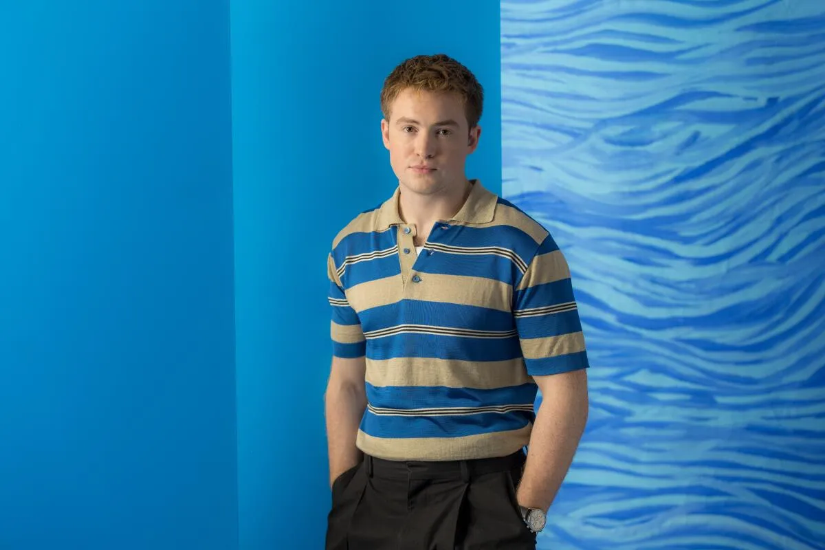 Kit Connor posando de cuerpo entero en una sesión de fotos con fondo azul