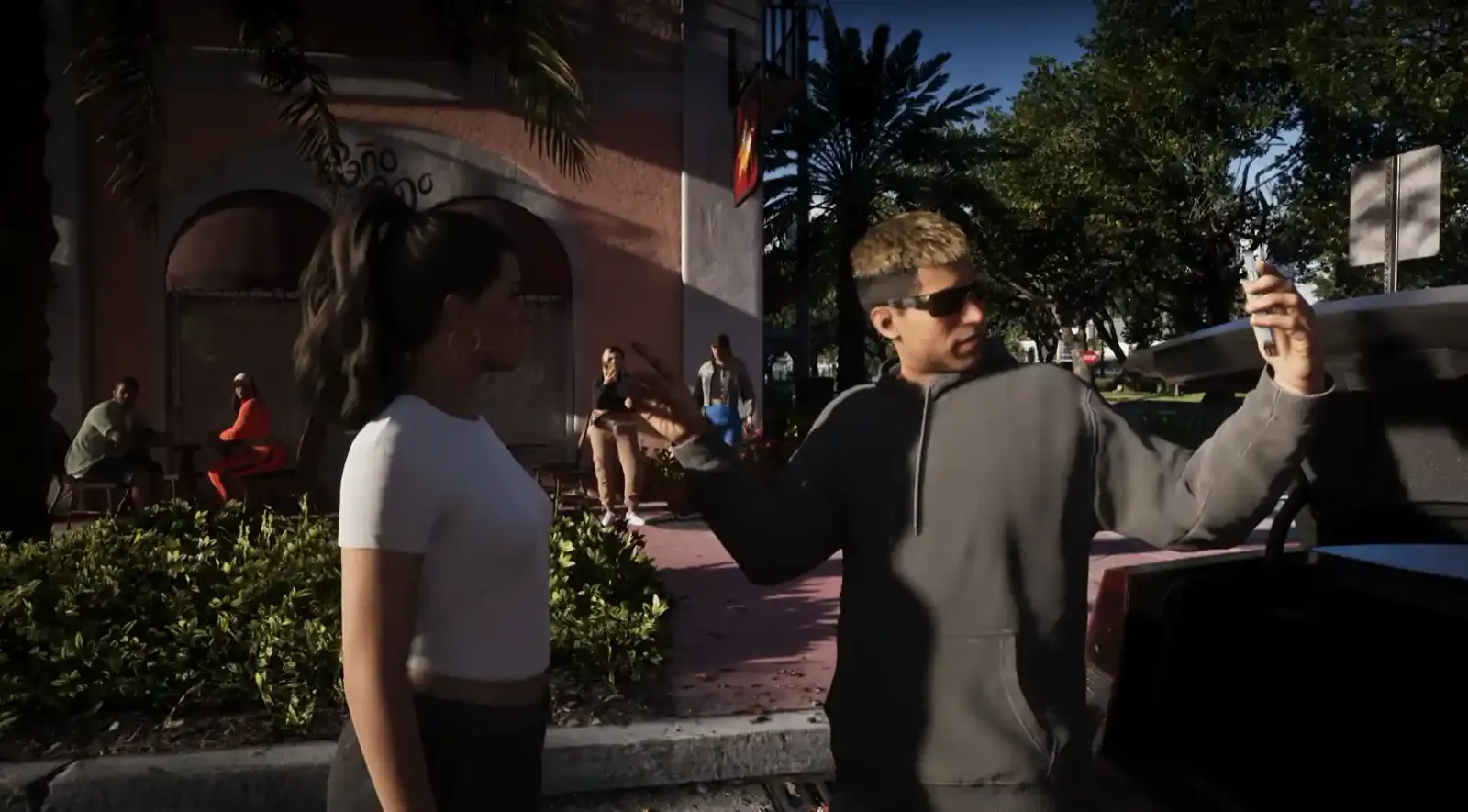 Jason y Lucia parados en una calle de Vice City rodeados de NPC, con Jason sosteniendo un teléfono, en GTA 6