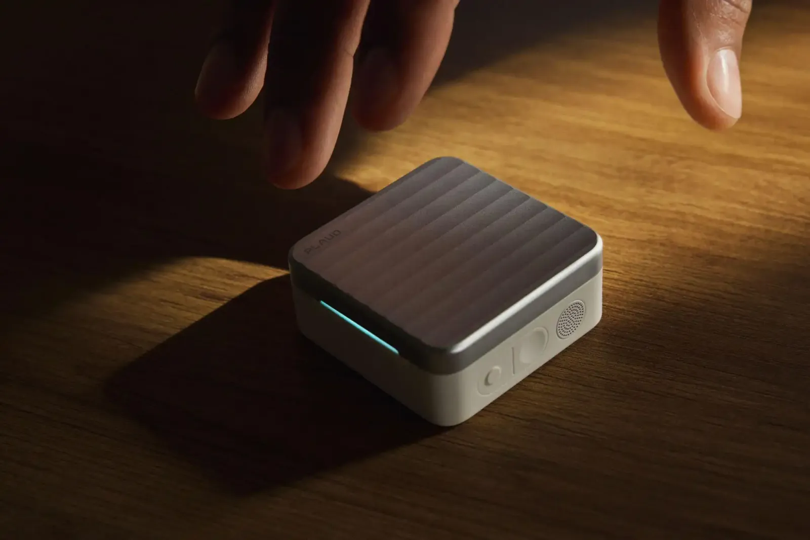 El estuche de los Plaud One apoyado sobre una mesa de madera con su luz encendida