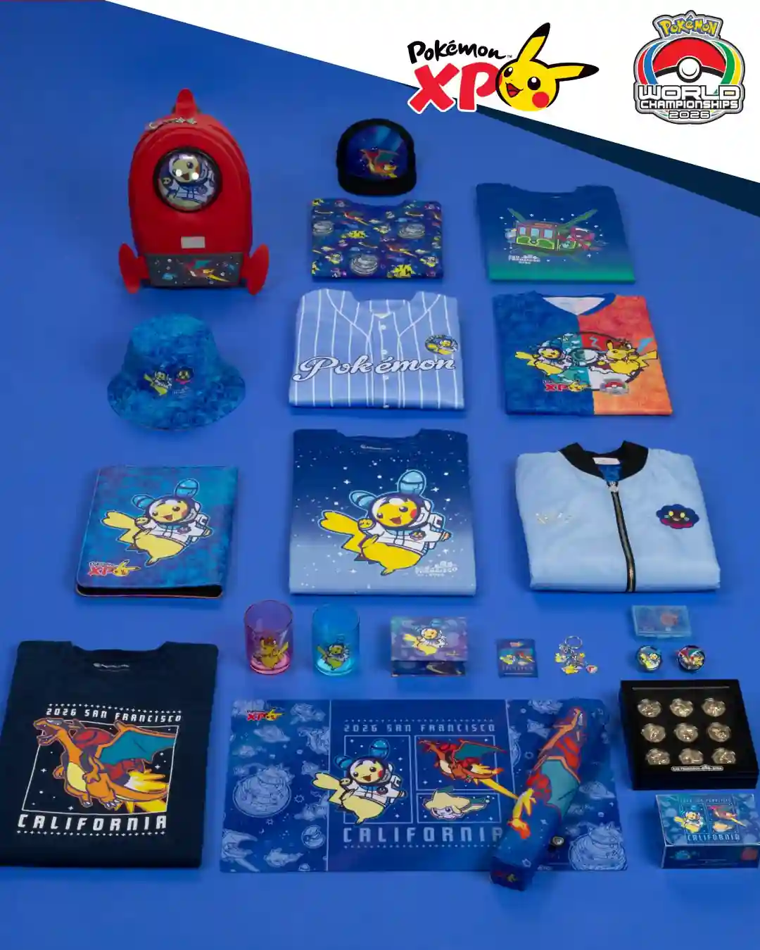 Línea PokémonXP del Pokémon Center Worlds 2026 con mochila cohete, gorra, remeras y pines sobre fondo azul