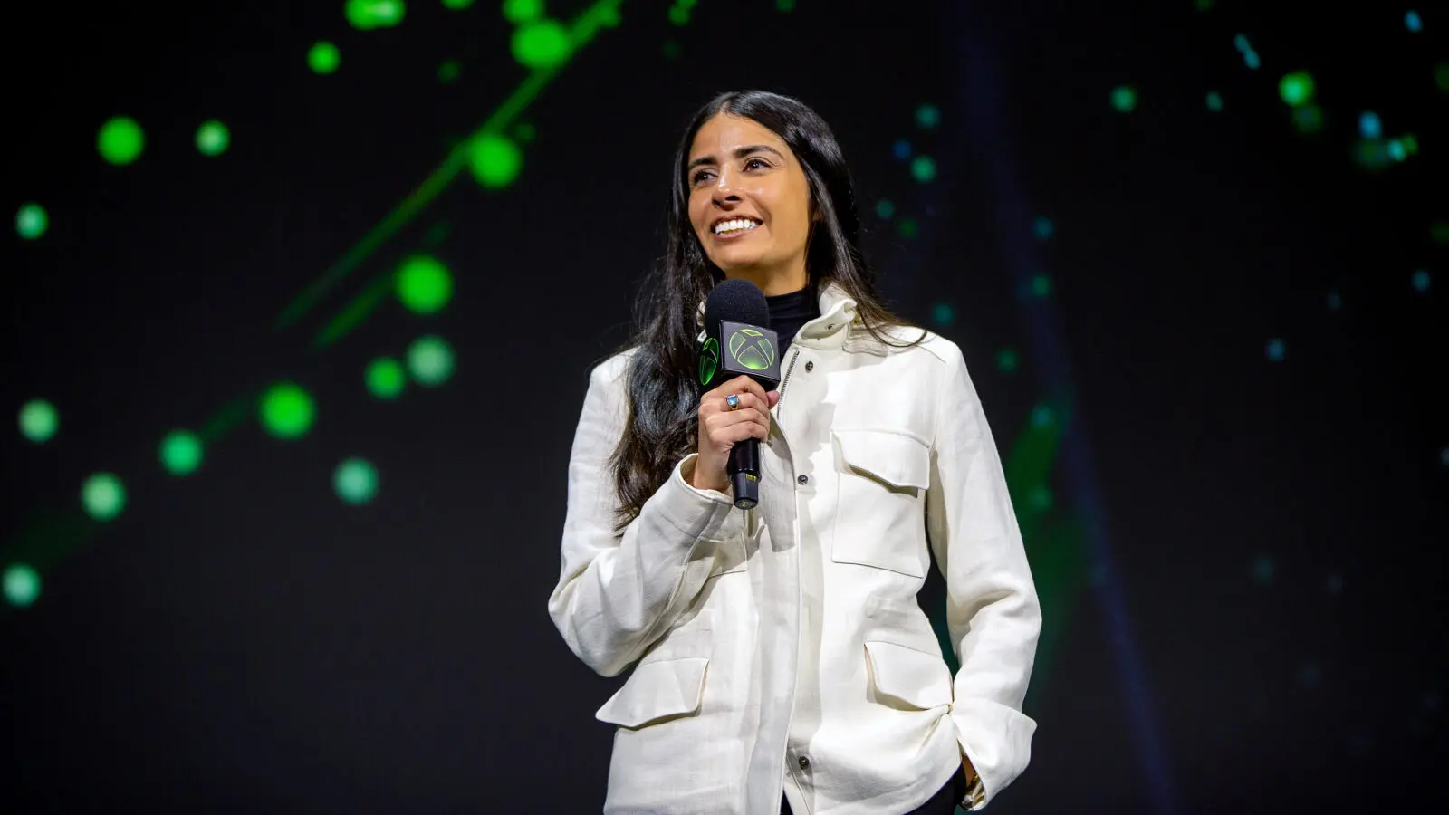 Asha Sharma, CEO de Xbox, habla en un escenario con un micrófono que lleva el logo verde de Xbox