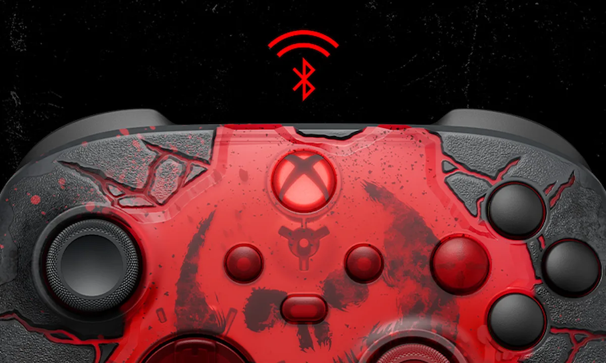 Detalle del control Xbox Gears of War E-Day con el ícono de Bluetooth en rojo y los botones translúcidos sobre el asfalto agrietado