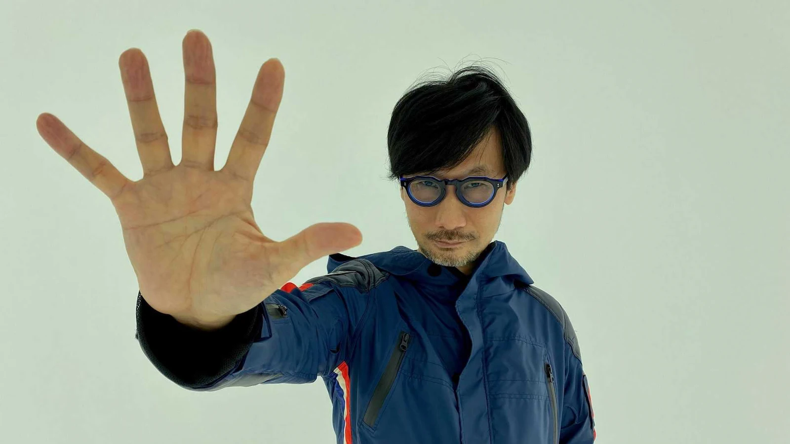 Hideo Kojima con la mano extendida hacia la cámara, en una foto promocional de Kojima Productions