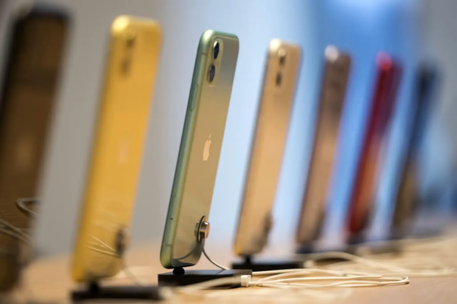 Varios iPhone de colores exhibidos en fila sobre una mesa de una tienda de Apple