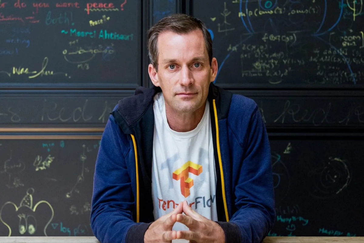 Jeff Dean, científico jefe de Google, con remera de TensorFlow frente a un pizarrón cubierto de ecuaciones