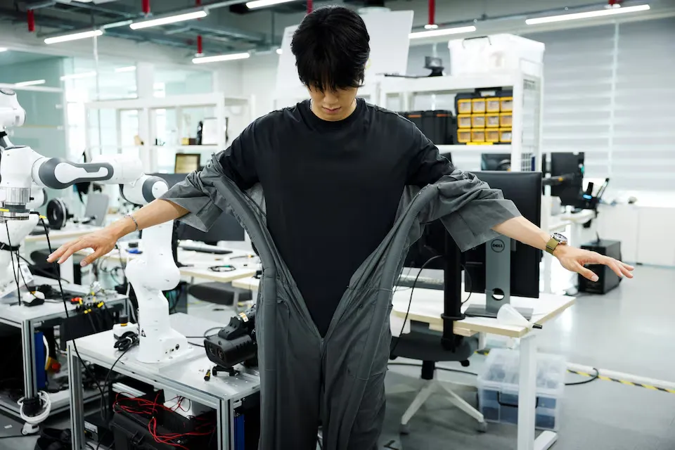 Un investigador de KAIST con los brazos extendidos mientras el robot le cierra solo un traje gris en el laboratorio