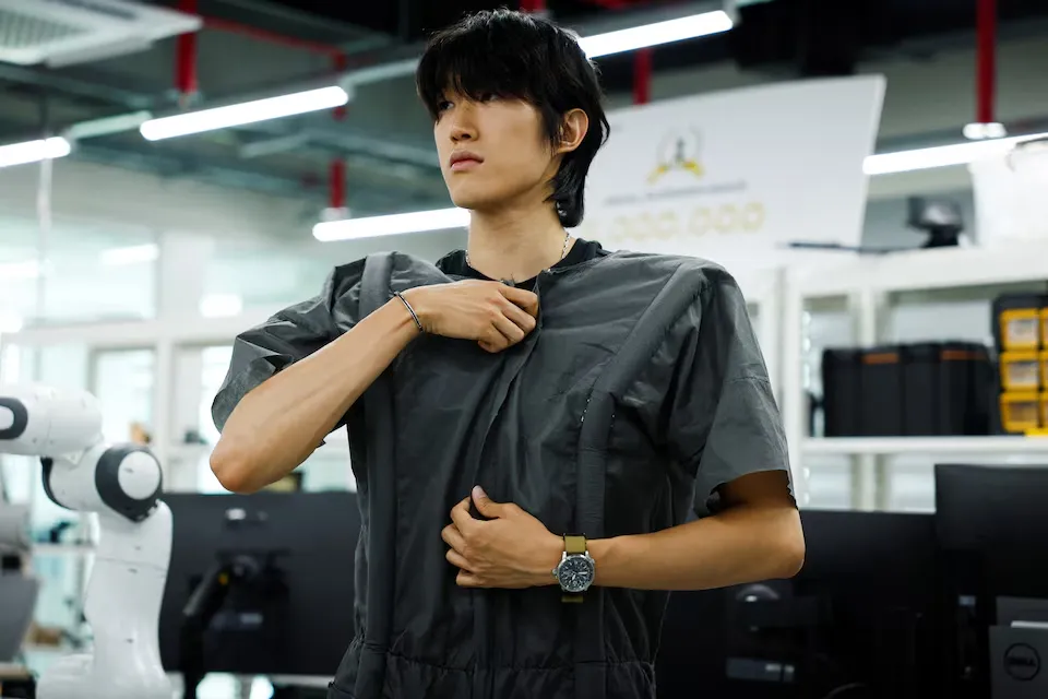 Un investigador de KAIST con el traje gris ya colocado por el robot, ajustándose el hombro en el laboratorio