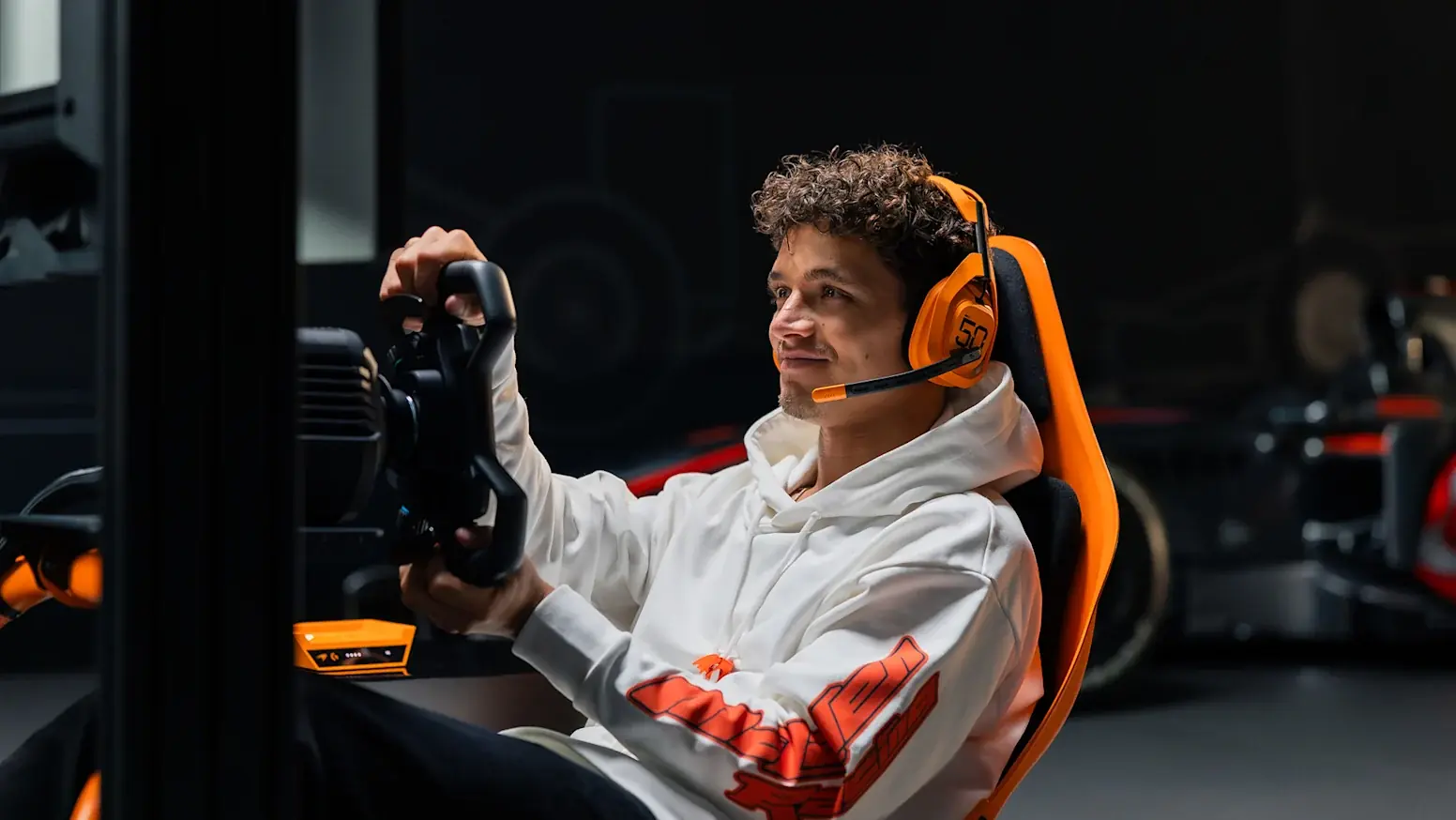 Lando Norris, piloto de McLaren, en una cabina de simulador papaya con auriculares y volante Logitech G