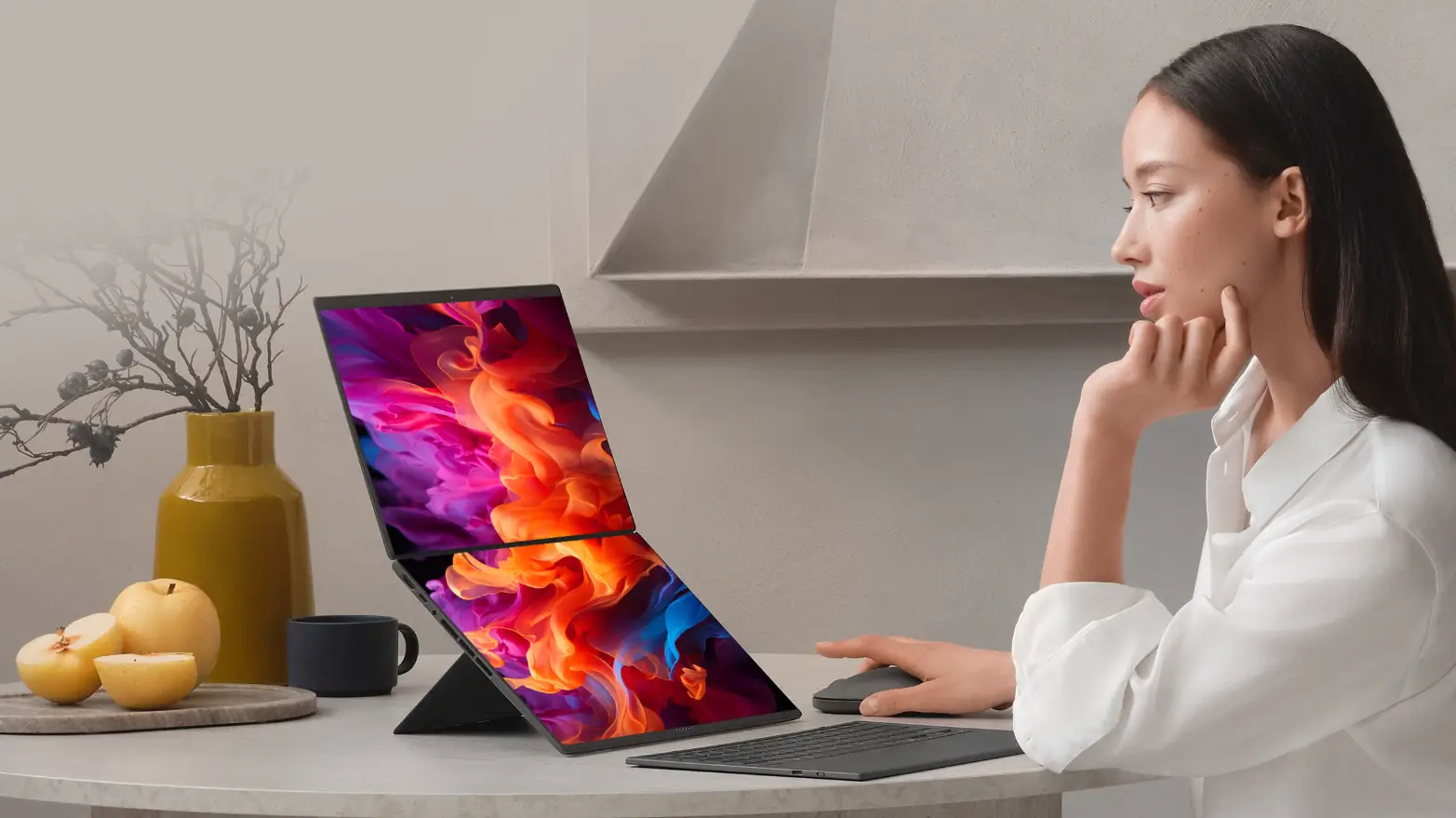 ASUS Zenbook DUO con las dos pantallas encendidas sobre su soporte, junto a una mujer en una cocina