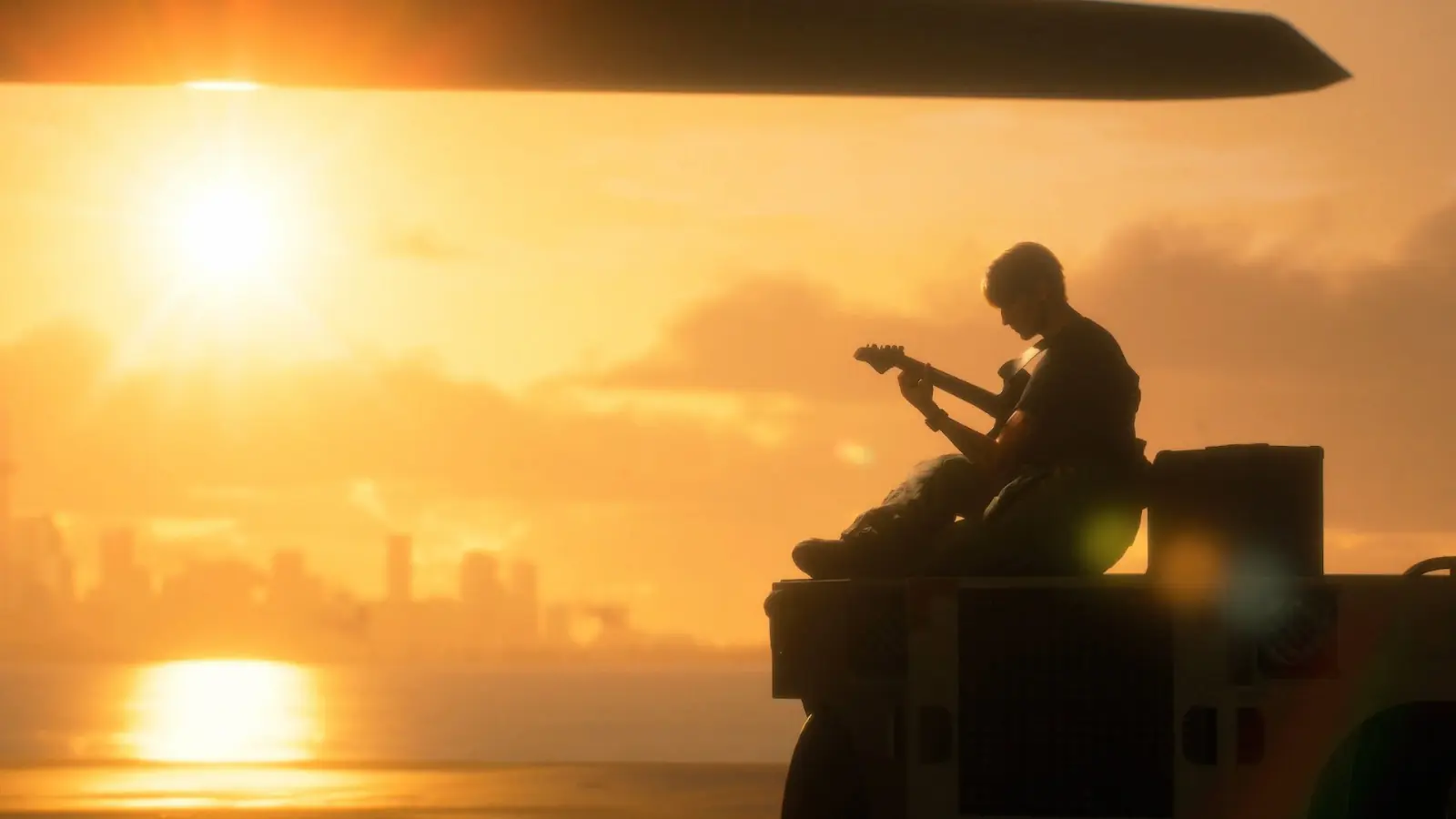 Un piloto toca la guitarra sentado sobre un vehículo de cubierta al atardecer, bajo el ala de un avión