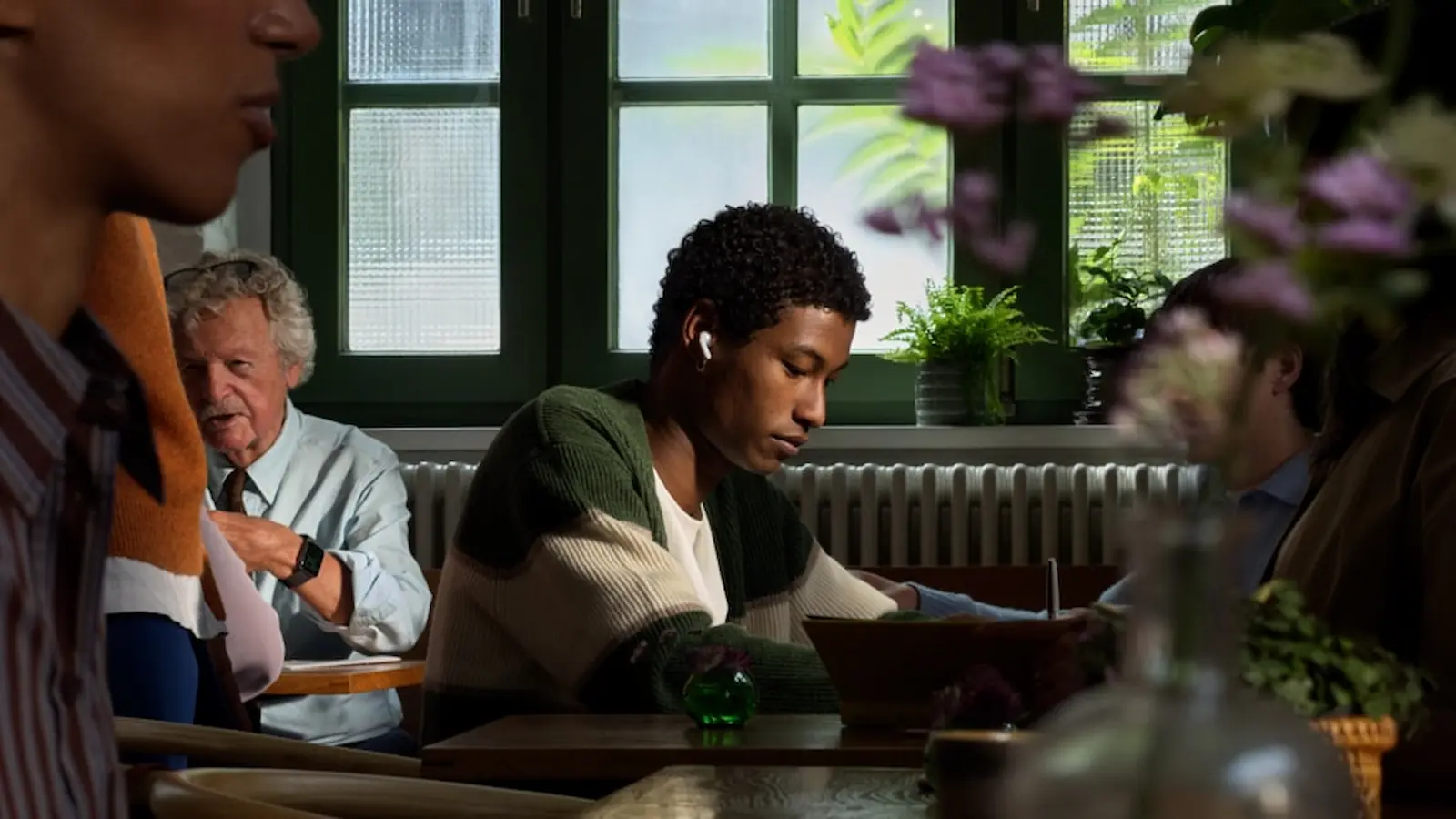 Una persona escuchando música con AirPods en un café. La denuncia apunta al procesamiento de audio de Apple, sin una lista pública de modelos