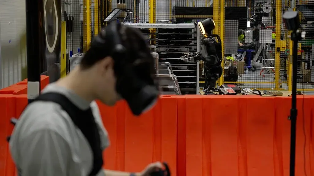Un operador con visor de realidad virtual entrena a un robot humanoide dentro de una planta industrial