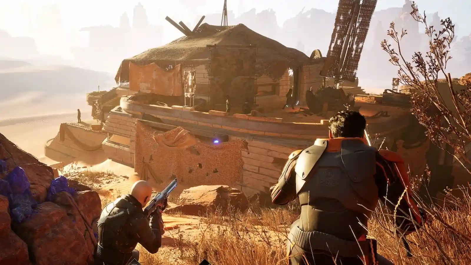 Dos jugadores armados avanzan hacia una base construida sobre la roca en Dune: Awakening