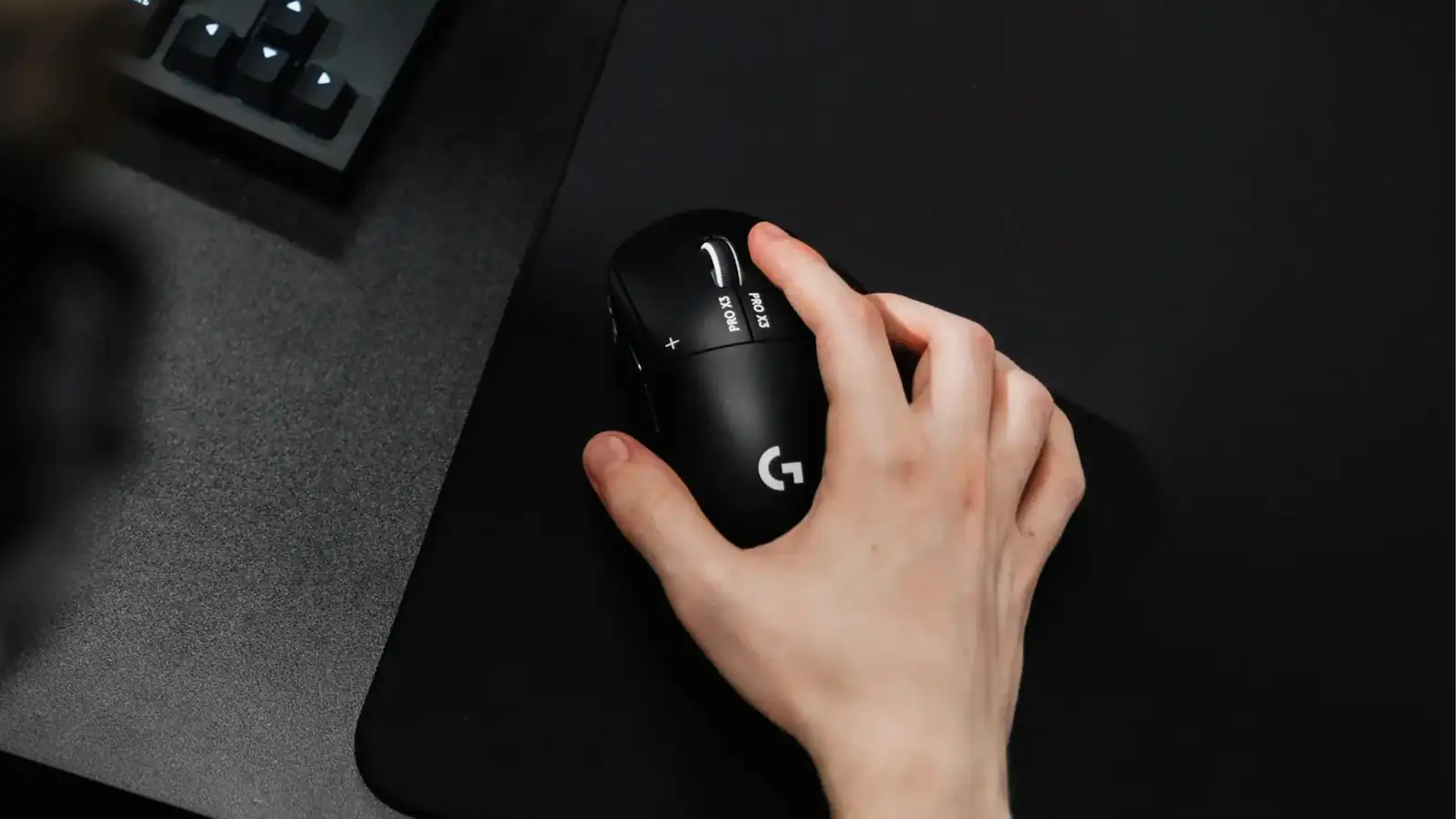 Mano apoyada sobre el mouse negro Logitech G PRO X3 SUPERSTRIKE en un escritorio