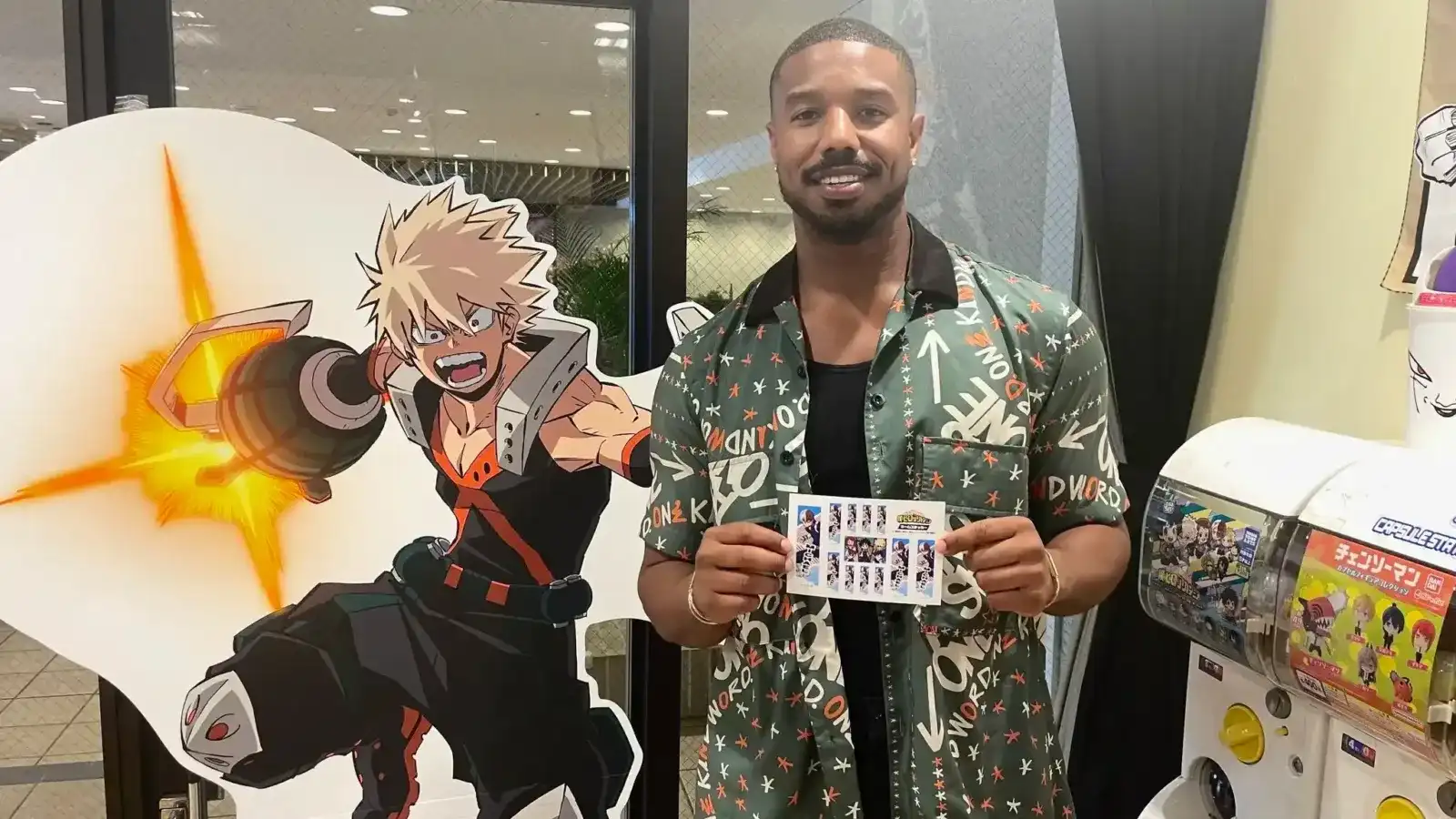 Michael B. Jordan posa junto a un recorte de cartón de Bakugo, de My Hero Academia, en un local con máquinas gashapon