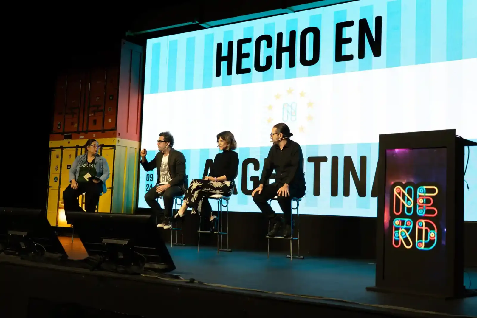 Panel en el escenario de Nerdearla con la pantalla Hecho en Argentina de fondo