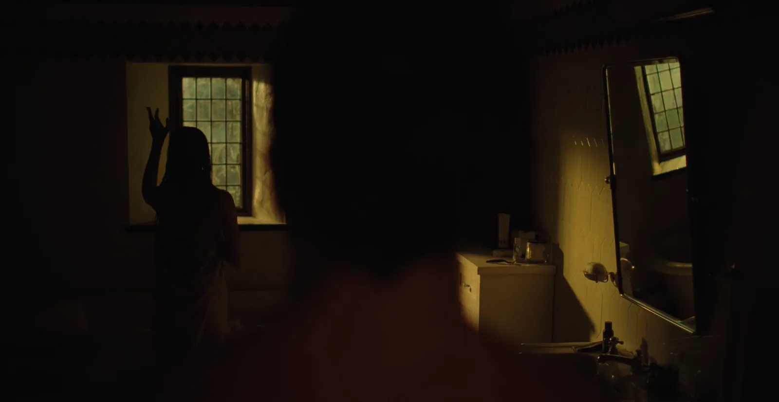 Tate de espaldas en un baño a oscuras, con Wren al fondo junto a la ventana, en el teaser de Nunca olvides que te quiero - Remain