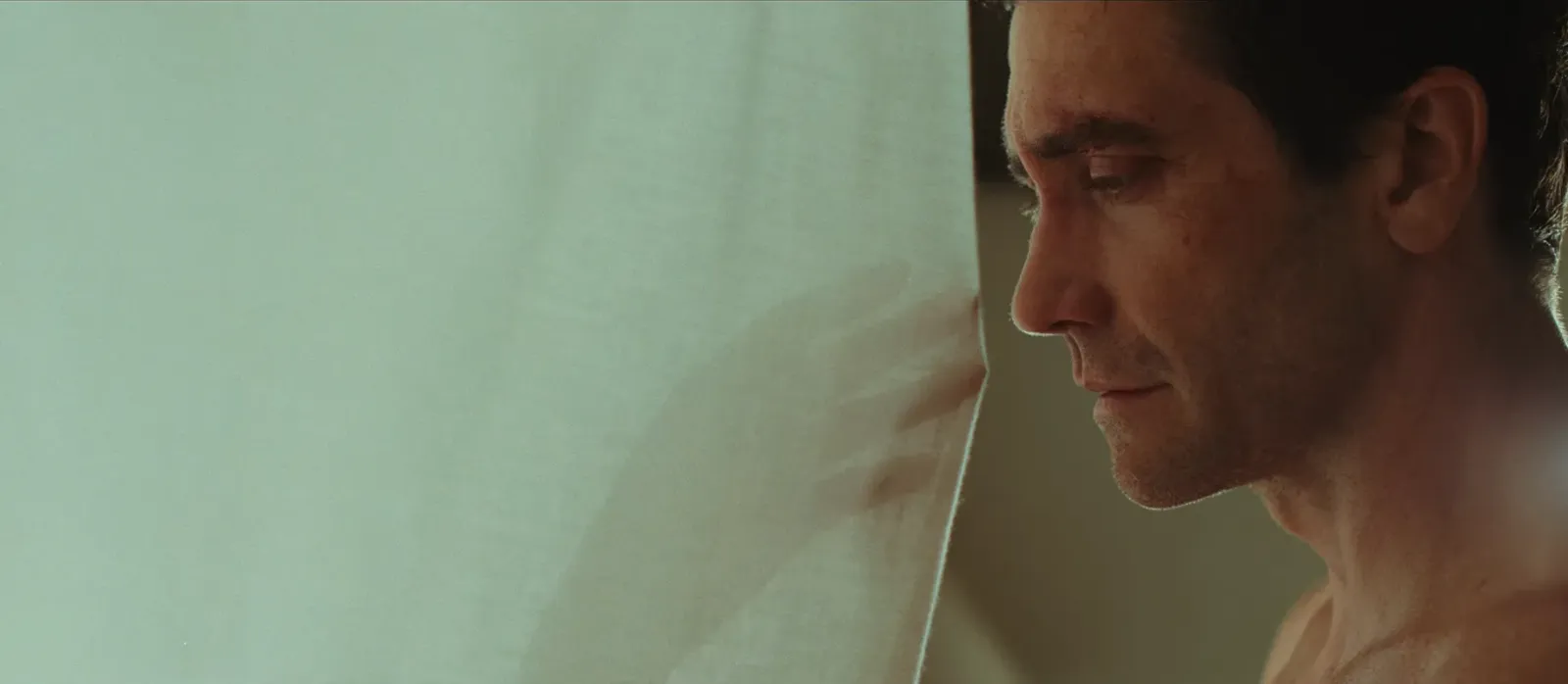 Jake Gyllenhaal de perfil junto a una cortina blanca en una escena del teaser de Remain o Nunca olvides que te quiero