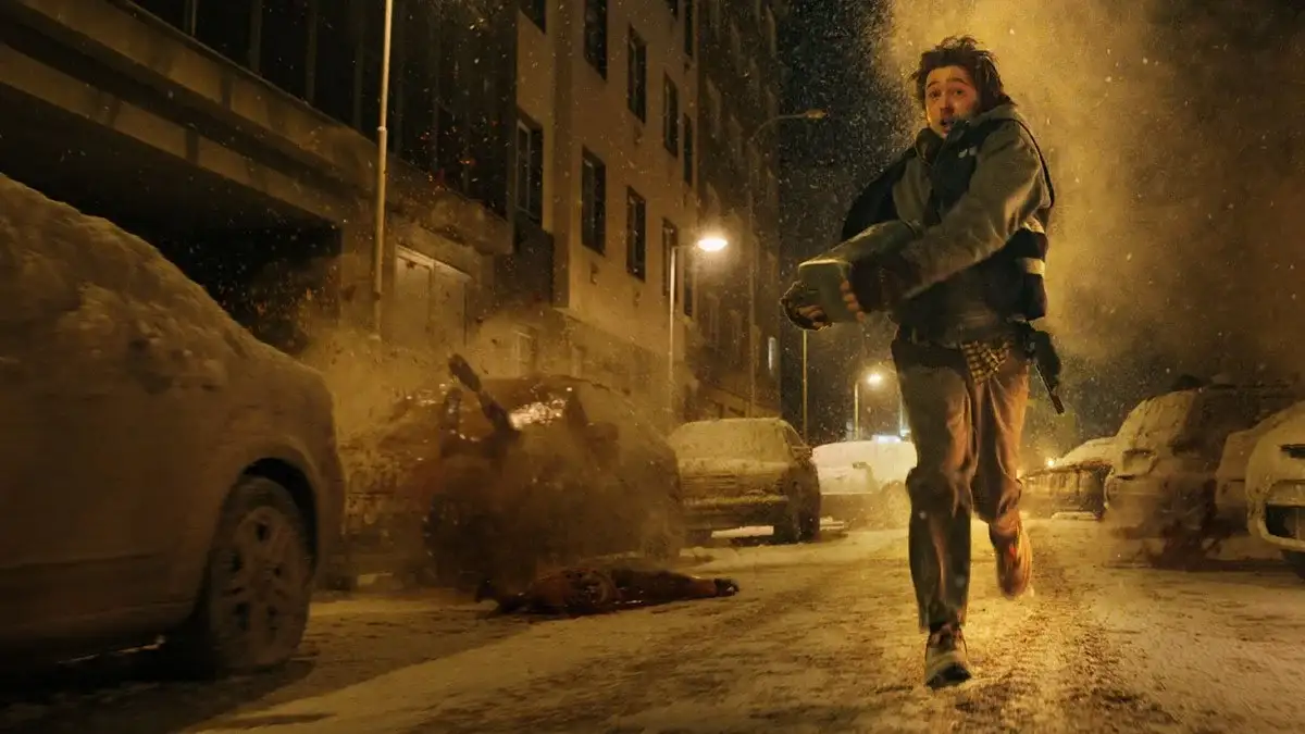 Austin Abrams corre por una calle nevada en una escena de Resident Evil: Noche Cero