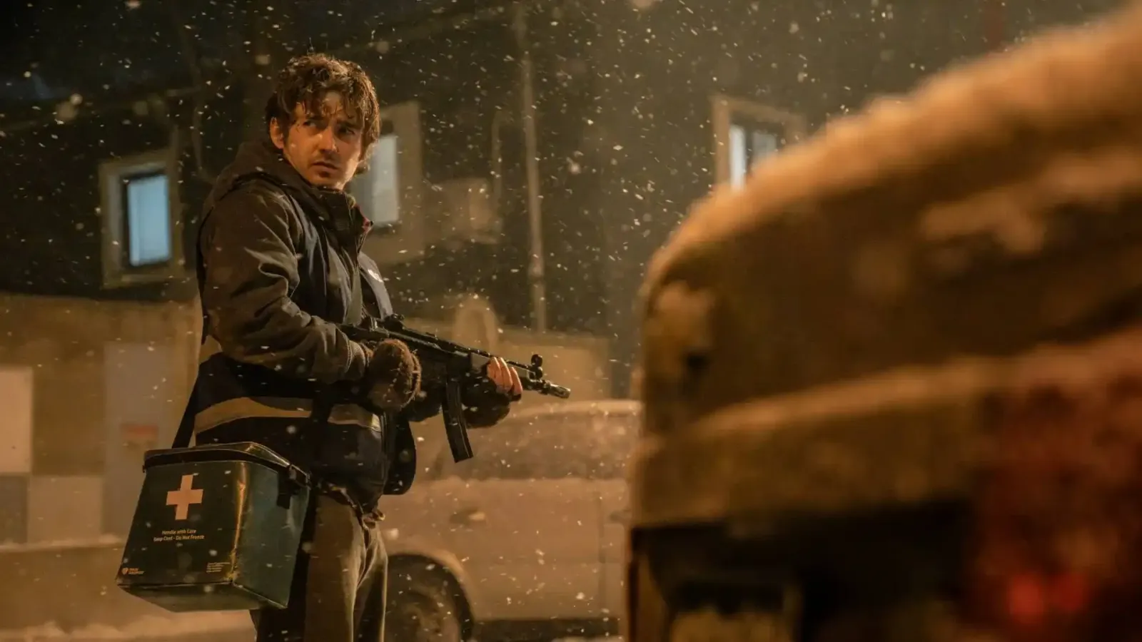 Austin Abrams con un arma y un botiquín en una calle nevada, en la película Resident Evil: Noche Cero
