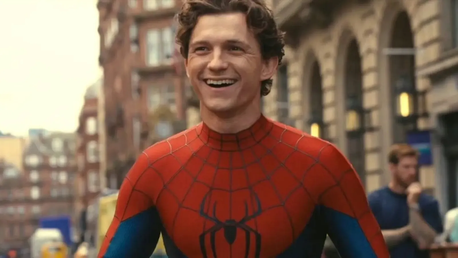 Tom Holland sonríe con el traje de Spider-Man, sin máscara, en una calle de la ciudad