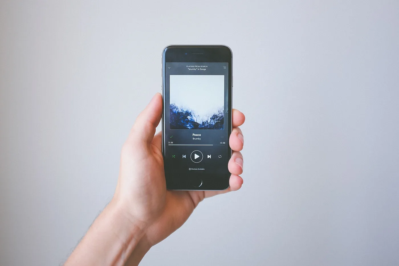 Una mano sostiene un celular con la aplicación de Spotify abierta sobre un fondo gris