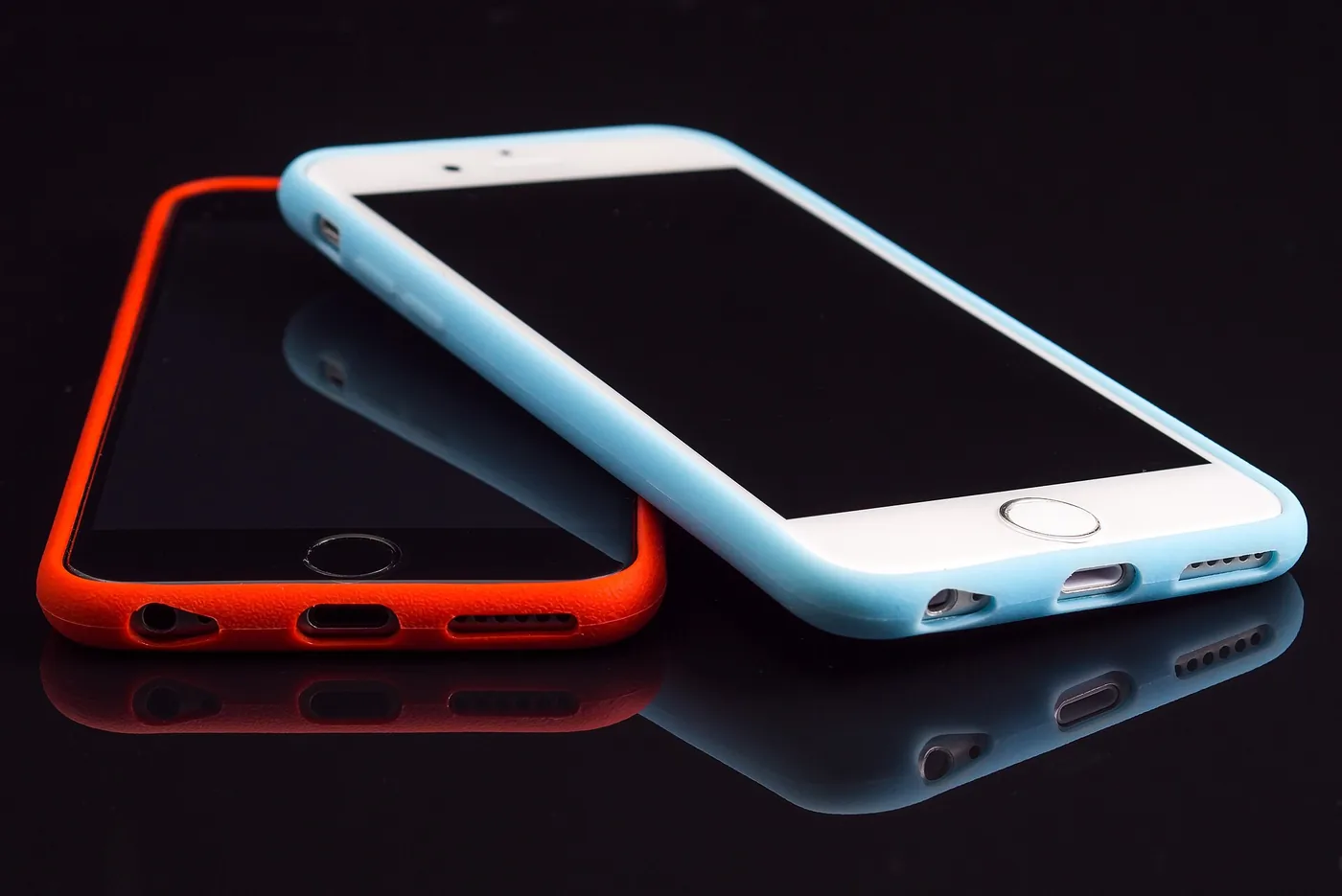 Dos iPhone, uno con funda roja y otro con funda celeste, apoyados uno sobre otro sobre una superficie negra