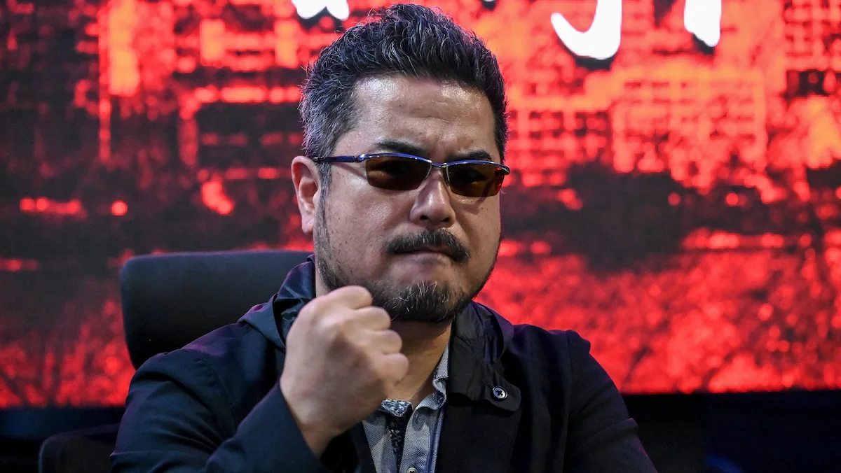 Katsuhiro Harada, CEO de VS Studio, con anteojos oscuros y el puño en alto sobre un fondo rojo