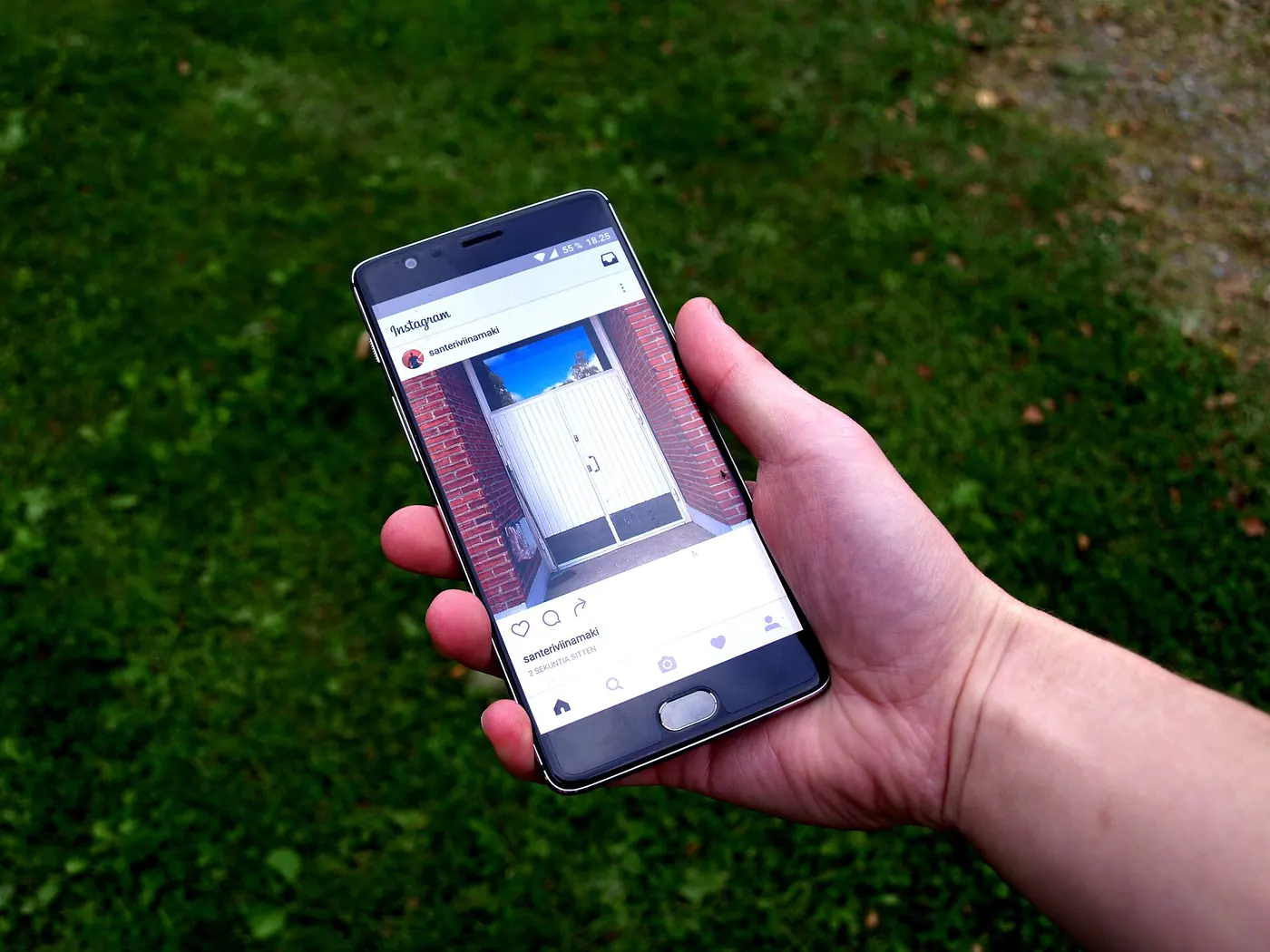 Una mano sostiene un celular con la aplicación de Instagram abierta, sobre un fondo de pasto