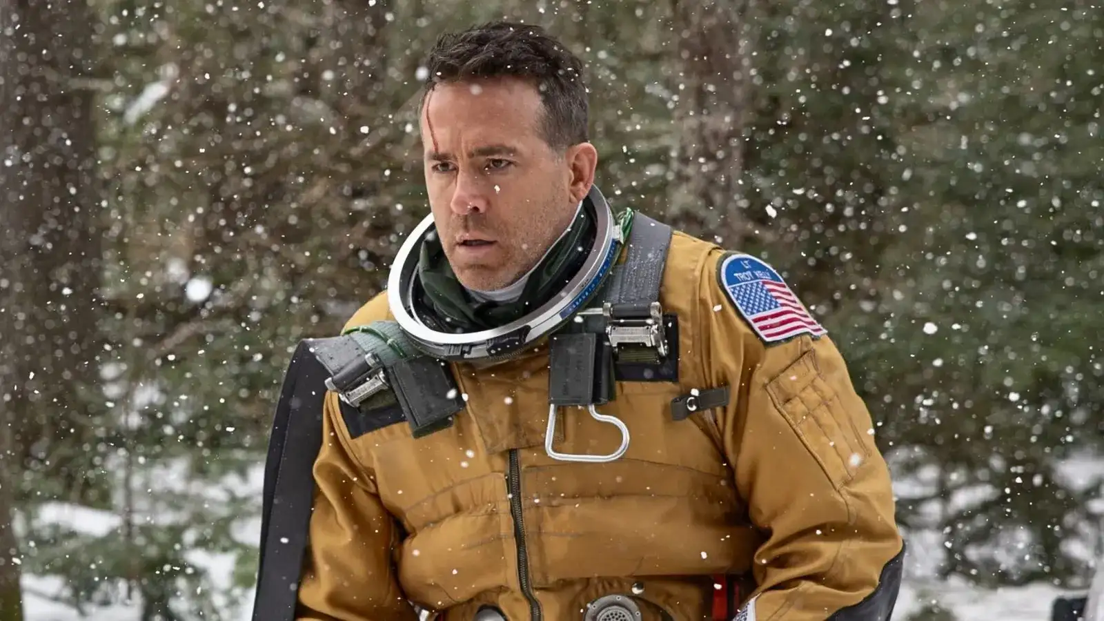 Ryan Reynolds con traje de vuelo y la bandera de Estados Unidos, bajo la nieve, en una escena de Mayday