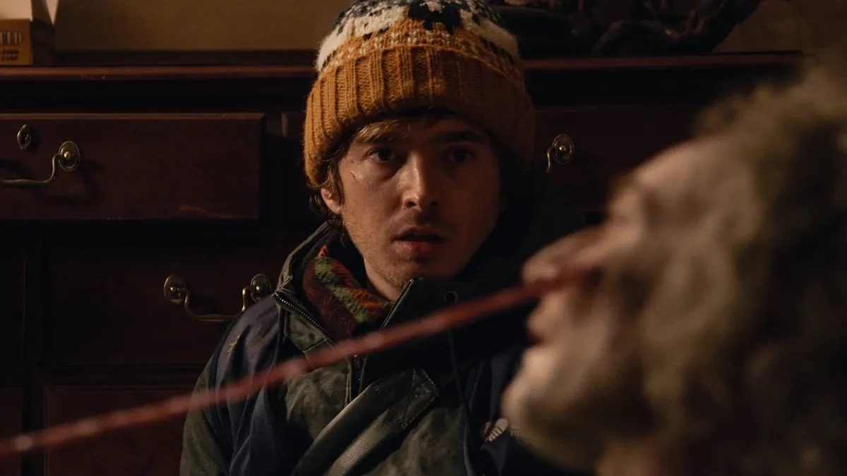 Austin Abrams con gorro de lana frente a una criatura en Resident Evil: Noche Cero, de Zach Cregger