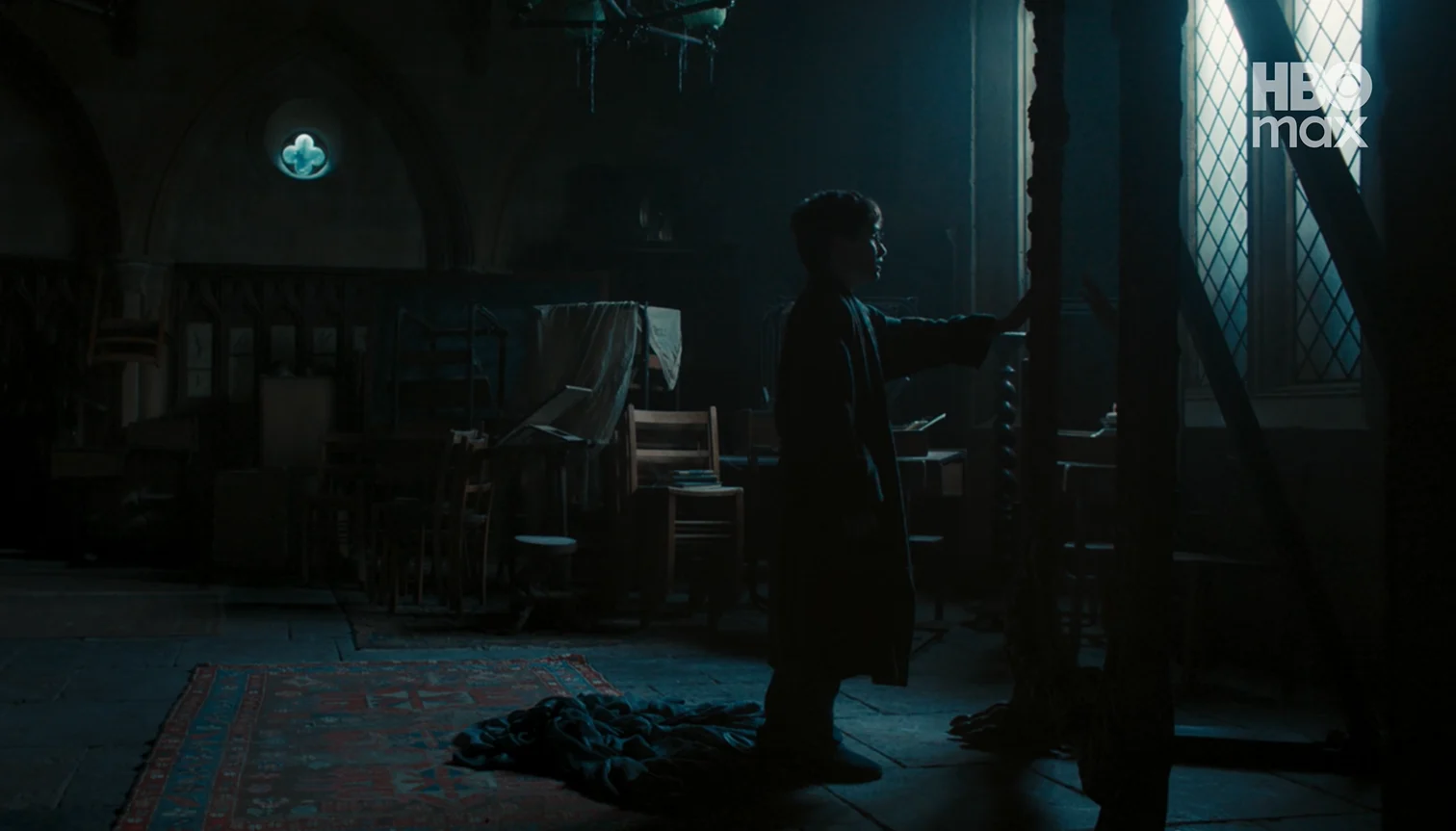 Harry Potter recorre de noche una sala en desuso de Hogwarts, con la capa de invisibilidad en el piso