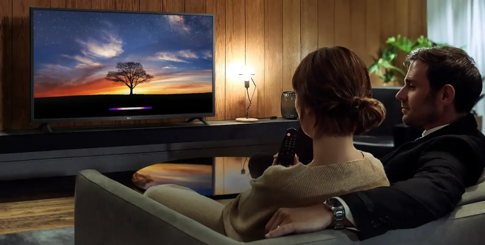 Pareja sentada en el sillón frente a un Smart TV de LG encendido en el living