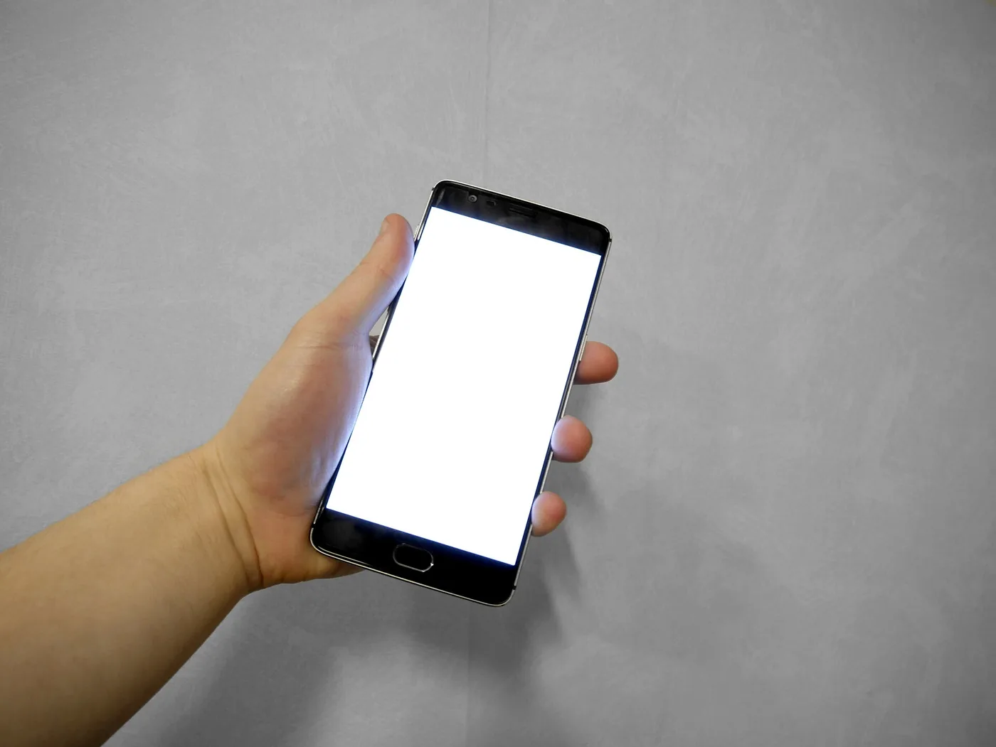 Una mano sostiene un smartphone con la pantalla en blanco sobre un fondo gris