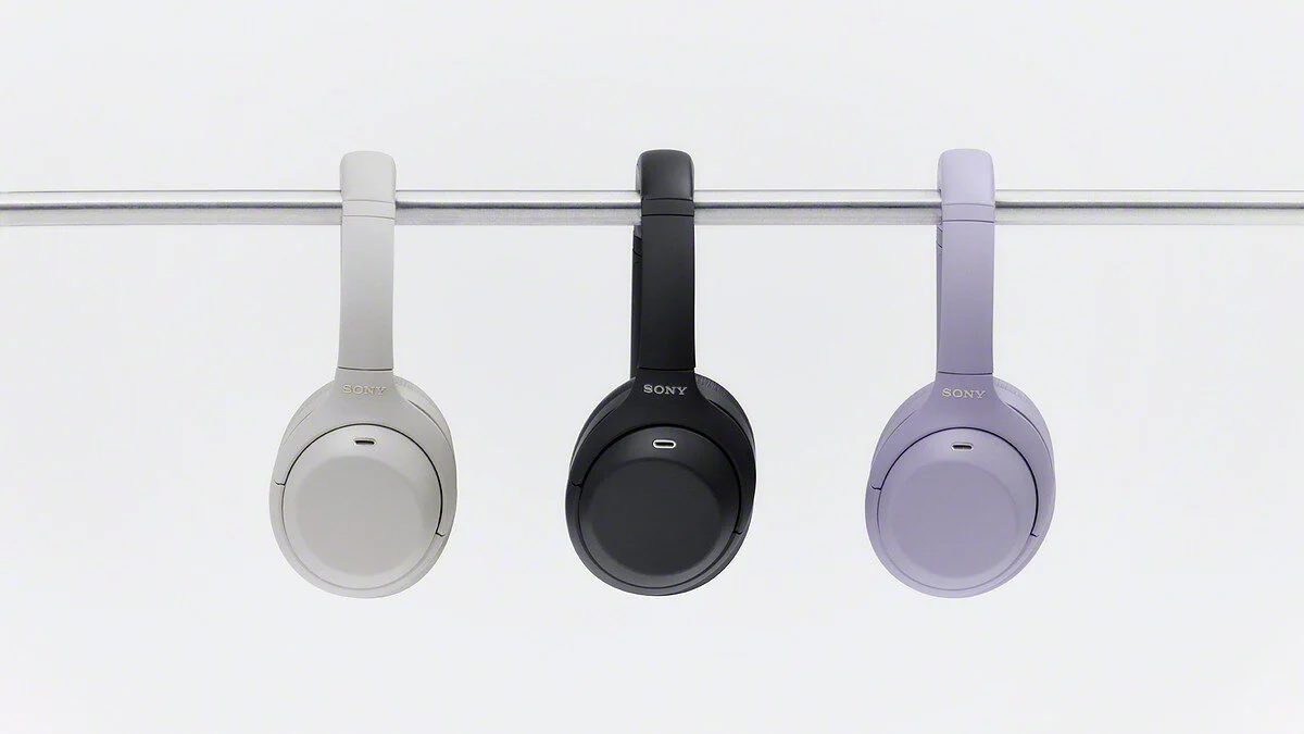 Tres auriculares Sony WH-1000XM4C colgados de una barra, en Platinum Silver, negro y lavanda