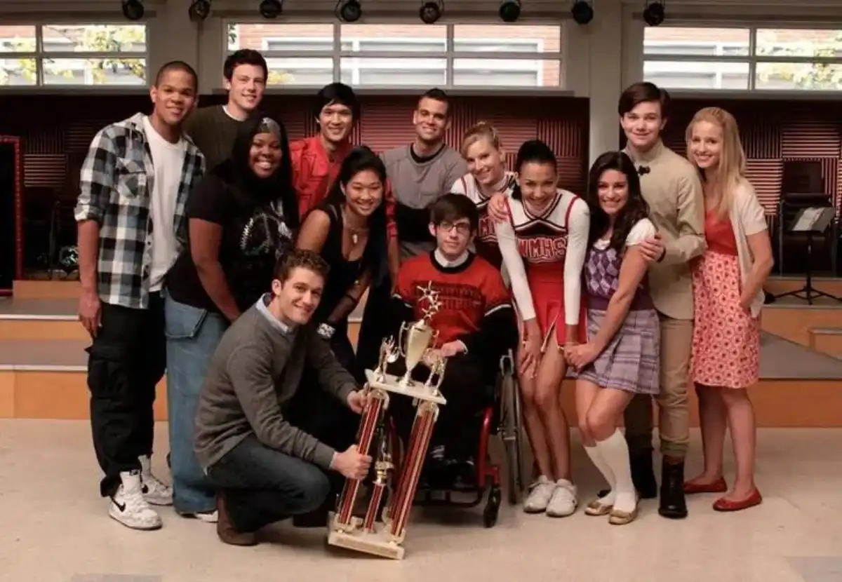 El elenco de Glee posa en la sala del coro junto al profesor Will Schuester (Matthew Morrison), que sostiene un trofeo de New Directions