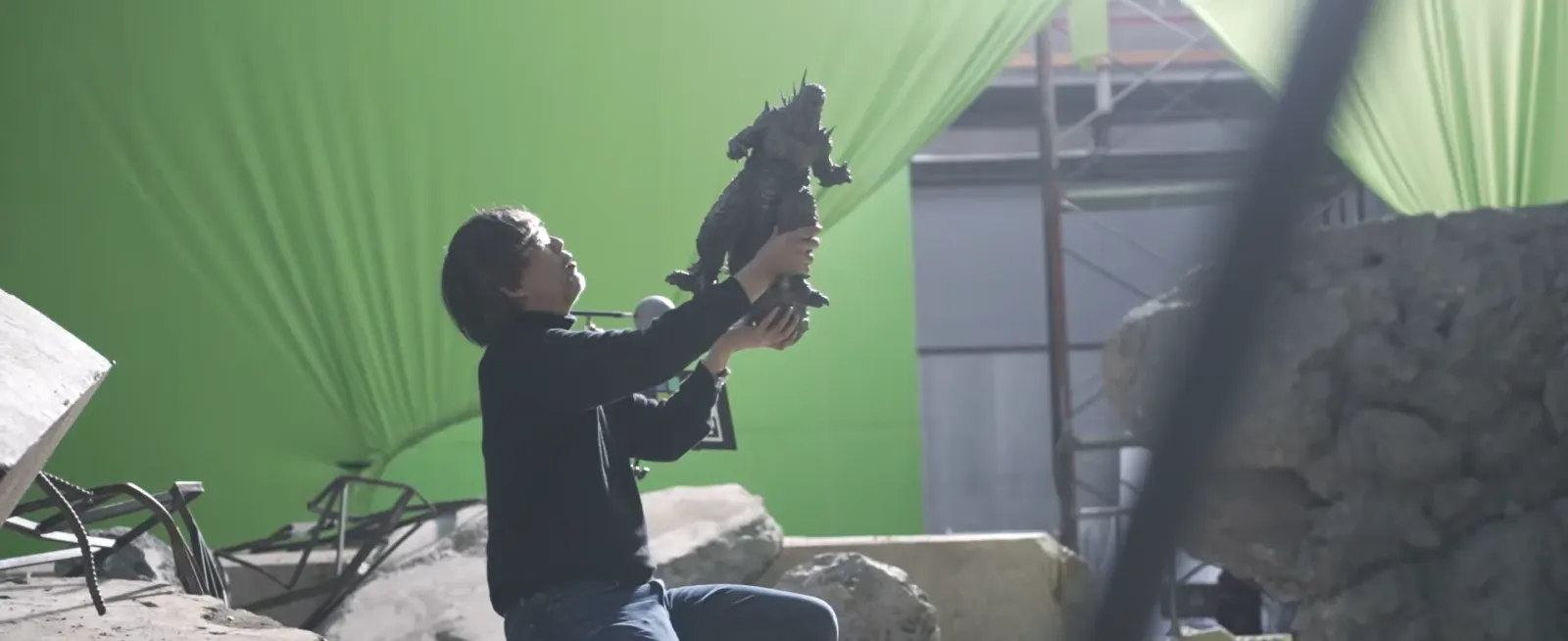 Takashi Yamazaki, director y guionista de Godzilla Minus Zero, sostiene una figura de Godzilla frente a una pantalla verde en un set de filmación