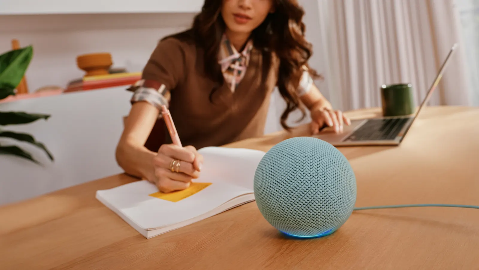 Nuevo Amazon Echo Dot verde agave sobre un escritorio junto a una mujer que escribe